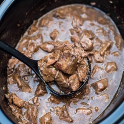A spoon scooping up beef tips and gravy from a slow cooker.