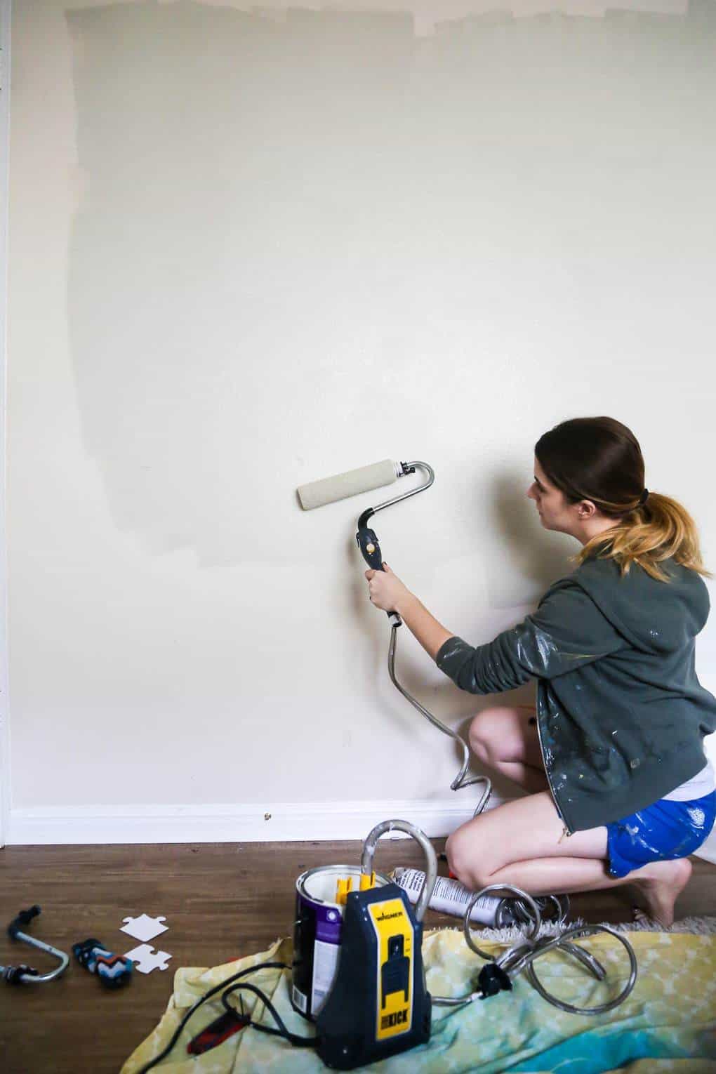 Woman painting a gray wall using a power roller