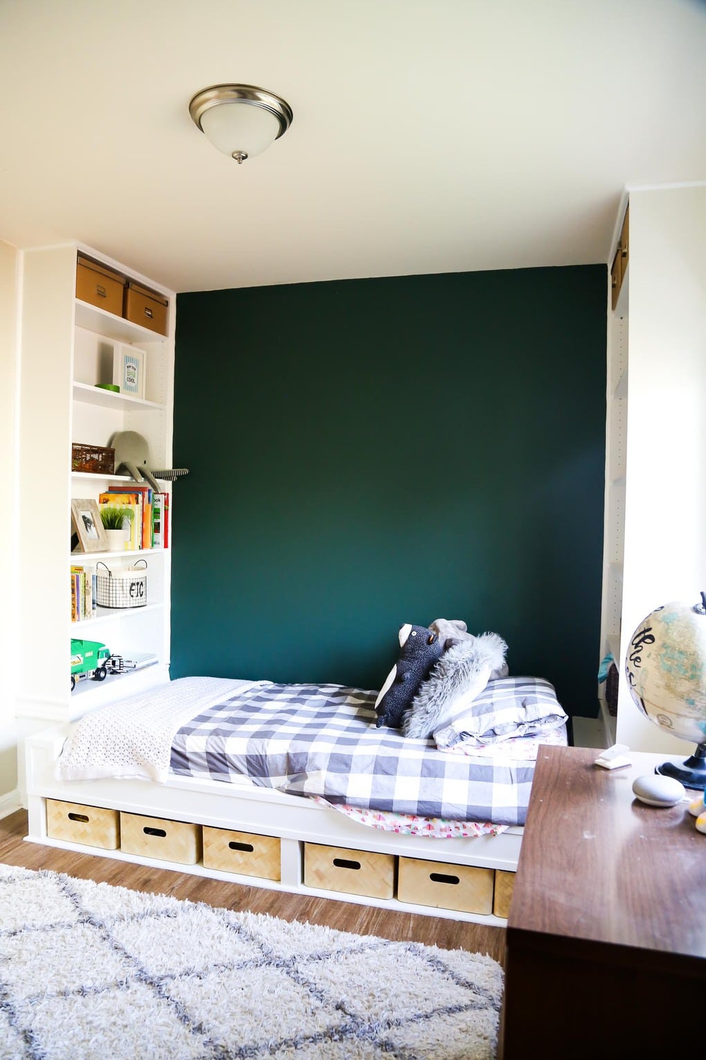 Build in shelves with a bed that has grey bedding and a green accent wall