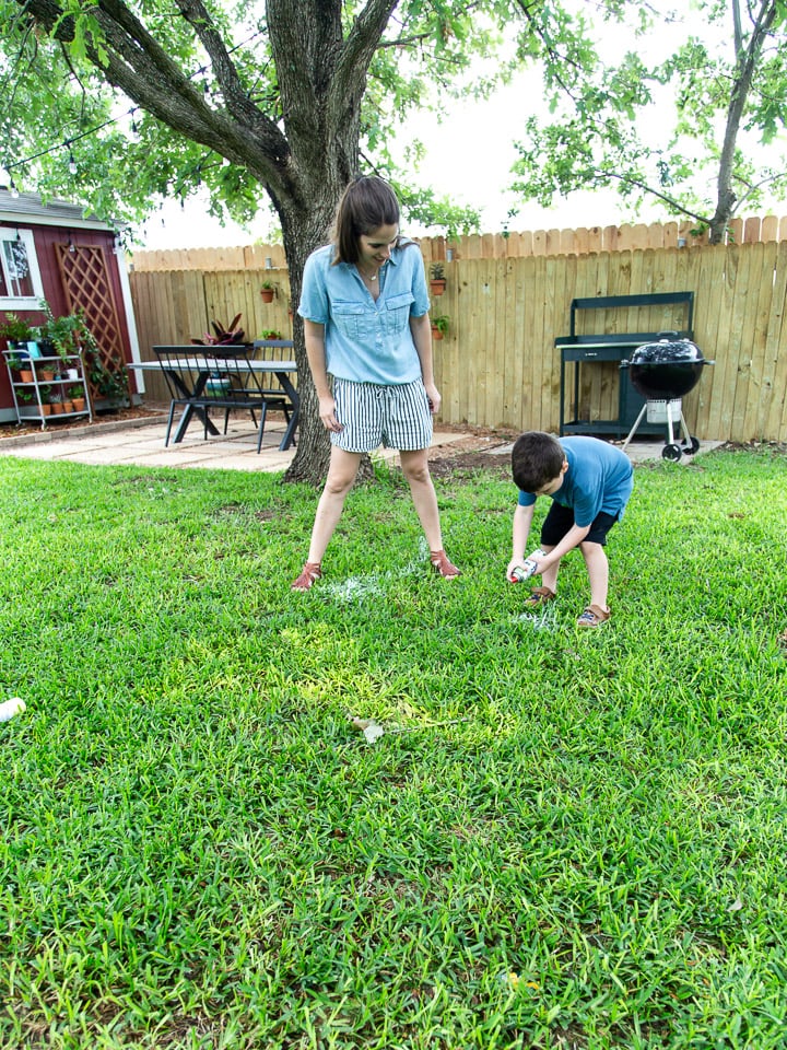 A mom and her young son playing Pictionary in the grass using spray chalk