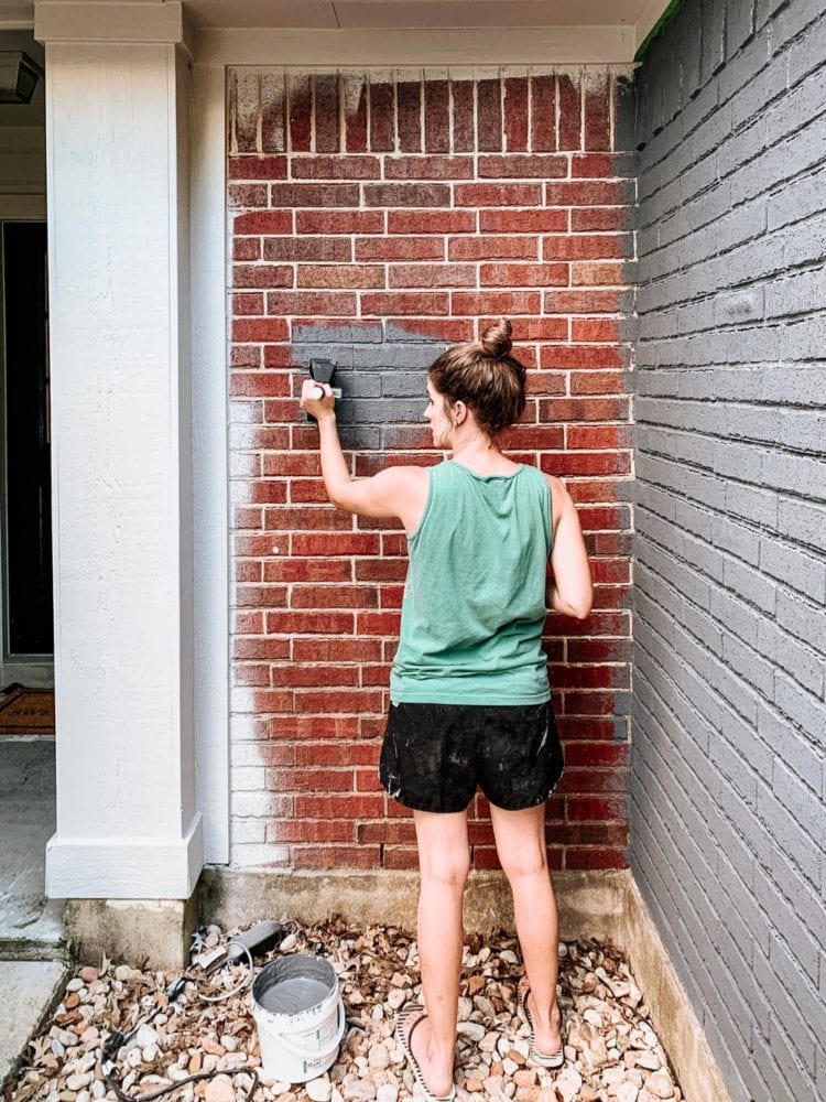 woman painting a red brick house with Romabio masonry paint in Navy Steel