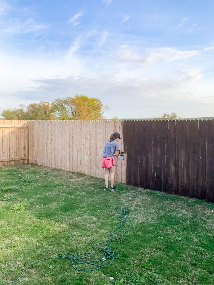 Woman staining a fence using a paint sprayer