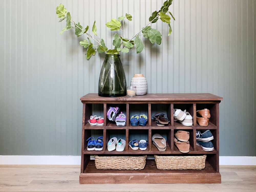 wooden shoe cubby in front of a dark green wall