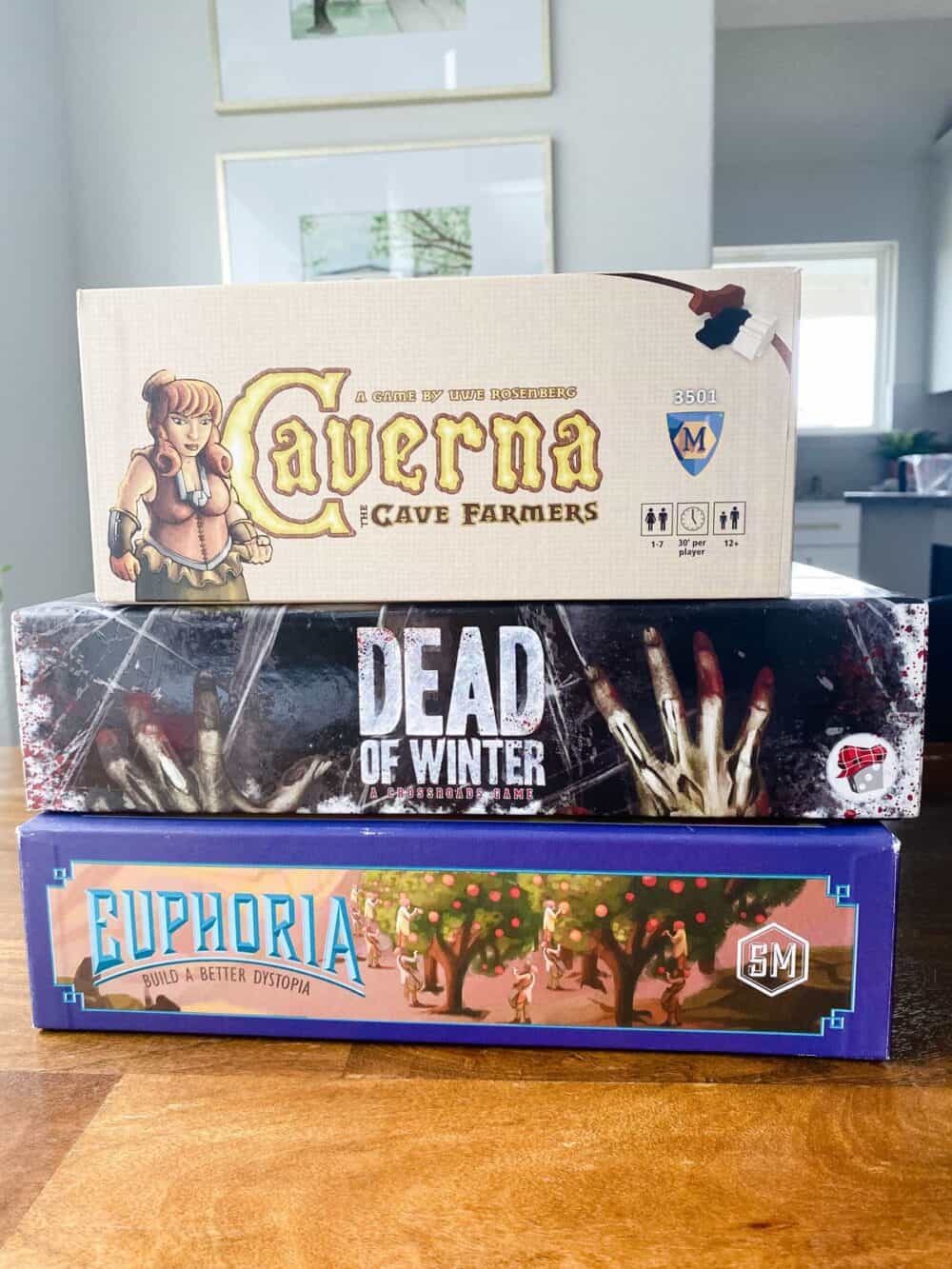 Stack of heavy board games, including Caverna, Dead of Winter, and Euphoria