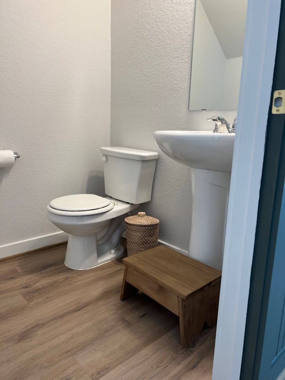 Small powder room with a wooden step stool in front of a pedestal sink 