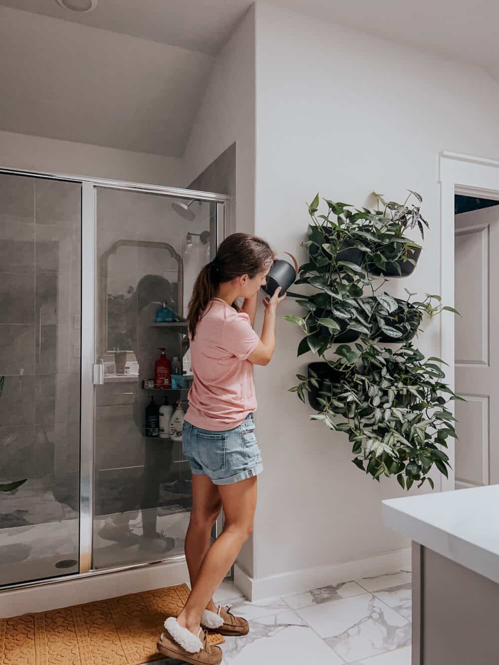 woman watering a wall of wall planters in a bathroom 