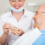 Smiling female dentist explaining artificial teeth to patient in clinic