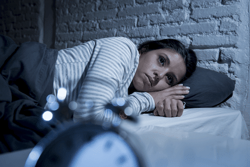 Woman lying in bed with insomnia, and could use help from a sleep coach for adults.