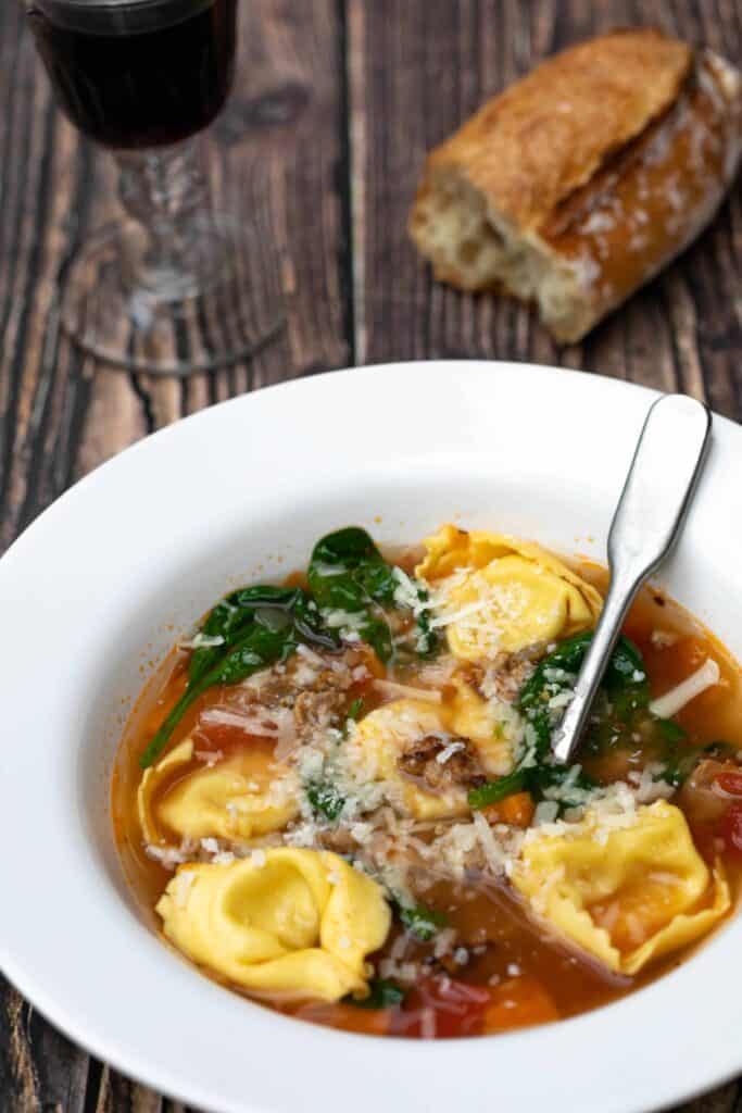 bowl of tuscan tortellini soup with glass of red wine and baguette