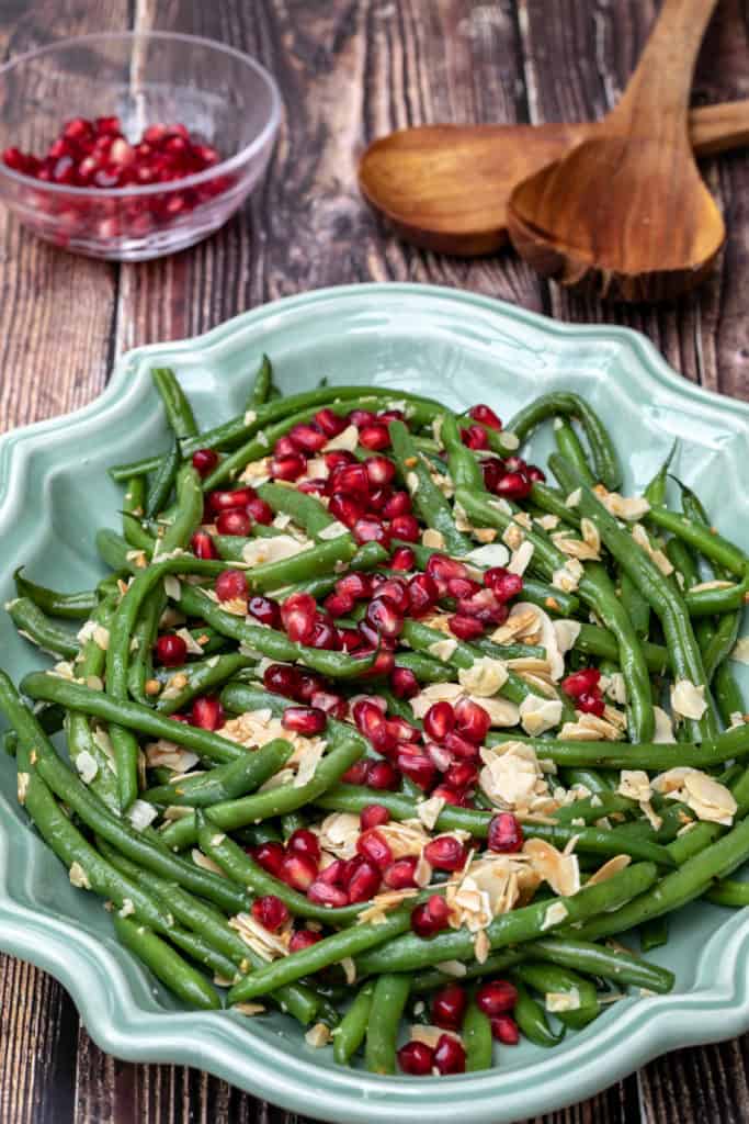green beans almondine with pomegranate seeds in large platter with seeds and tongs