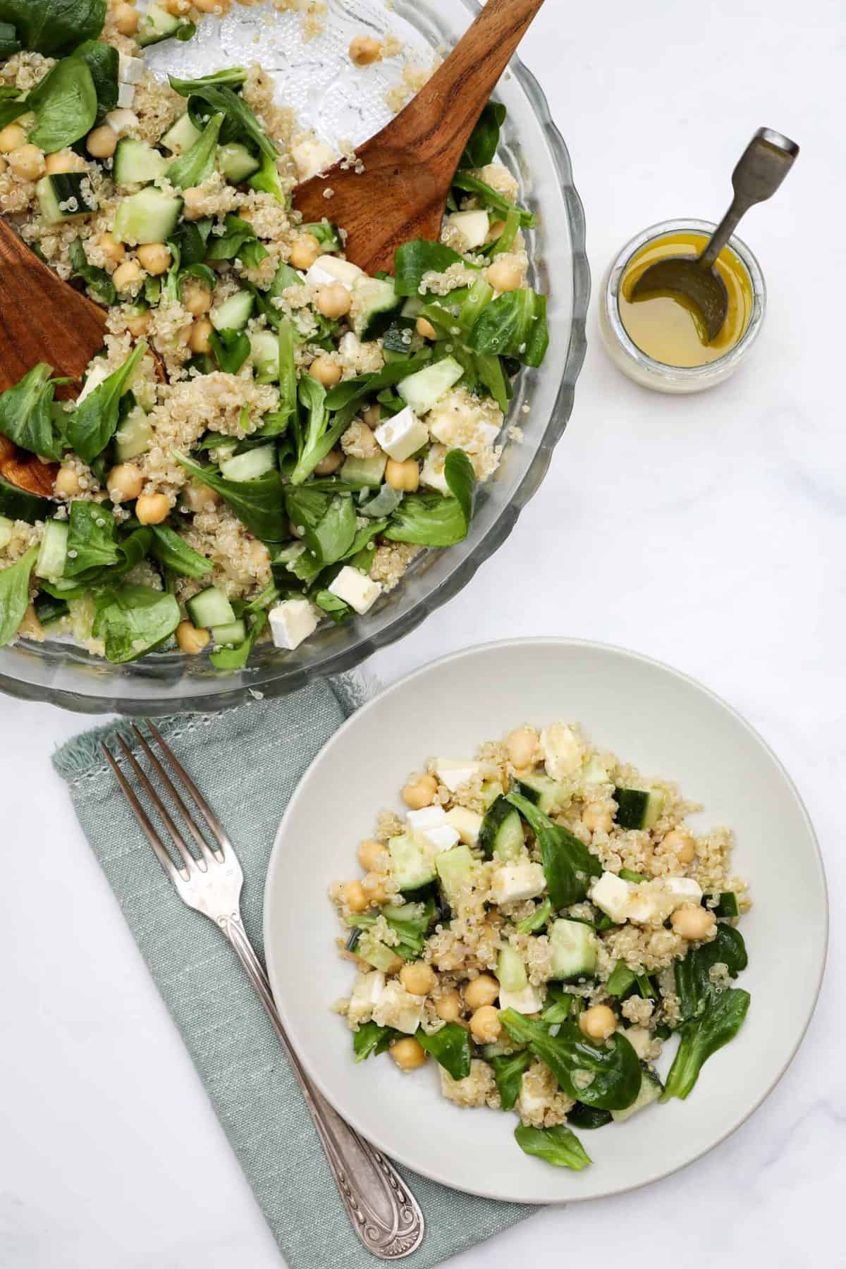 Plate of quinoa chickpea salad next to big bowl of salad and vinaigrette