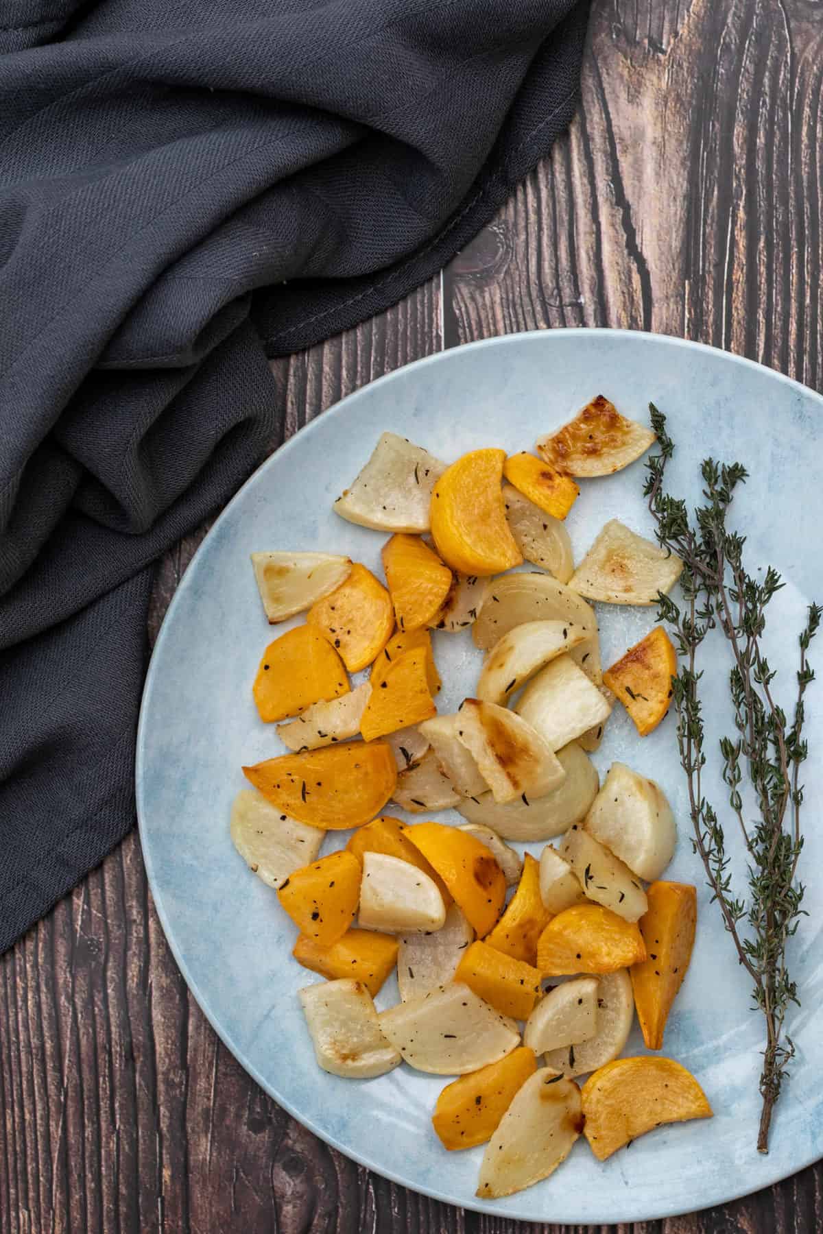 plate of roasted turnips with thyme on wooden background with towel