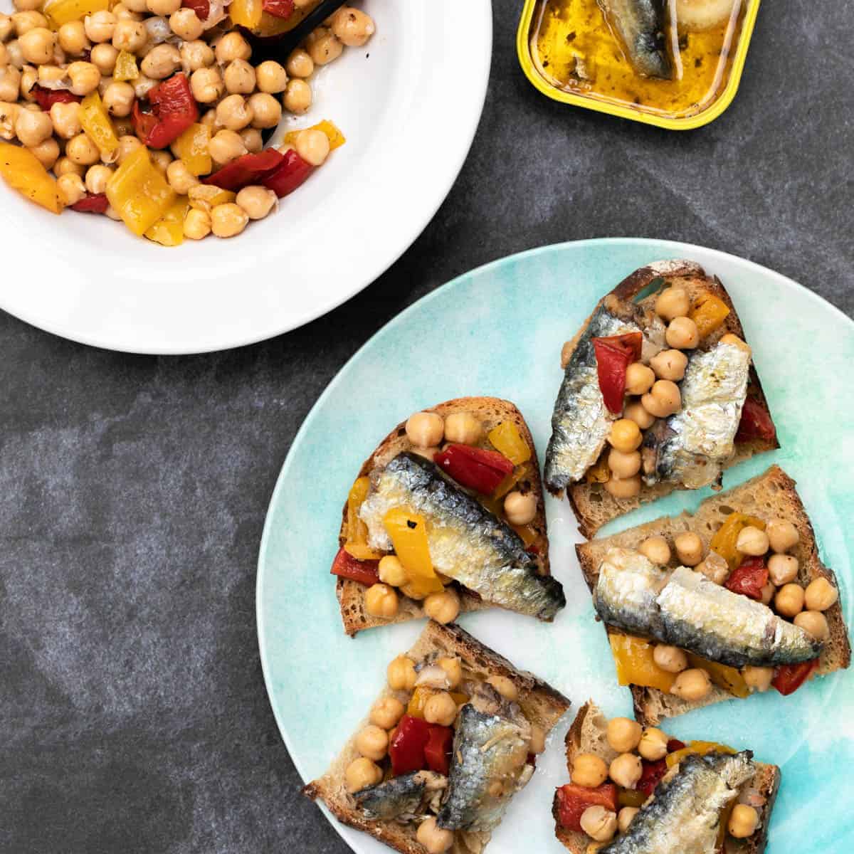 sardines on toast with chickpea salad on plate next to bowl of chickpea salad and sardine tin