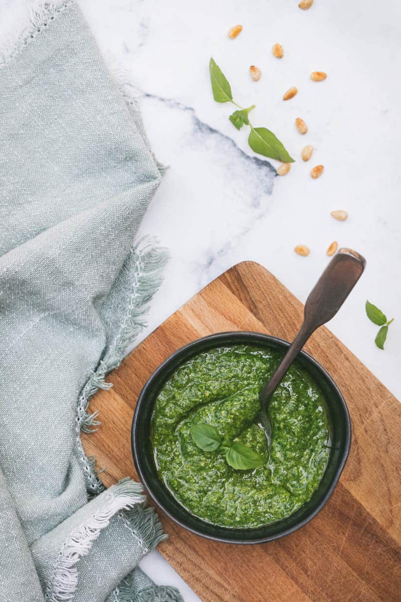 lemon basil pesto in small bowl on cutting board with spoon next to napkin
