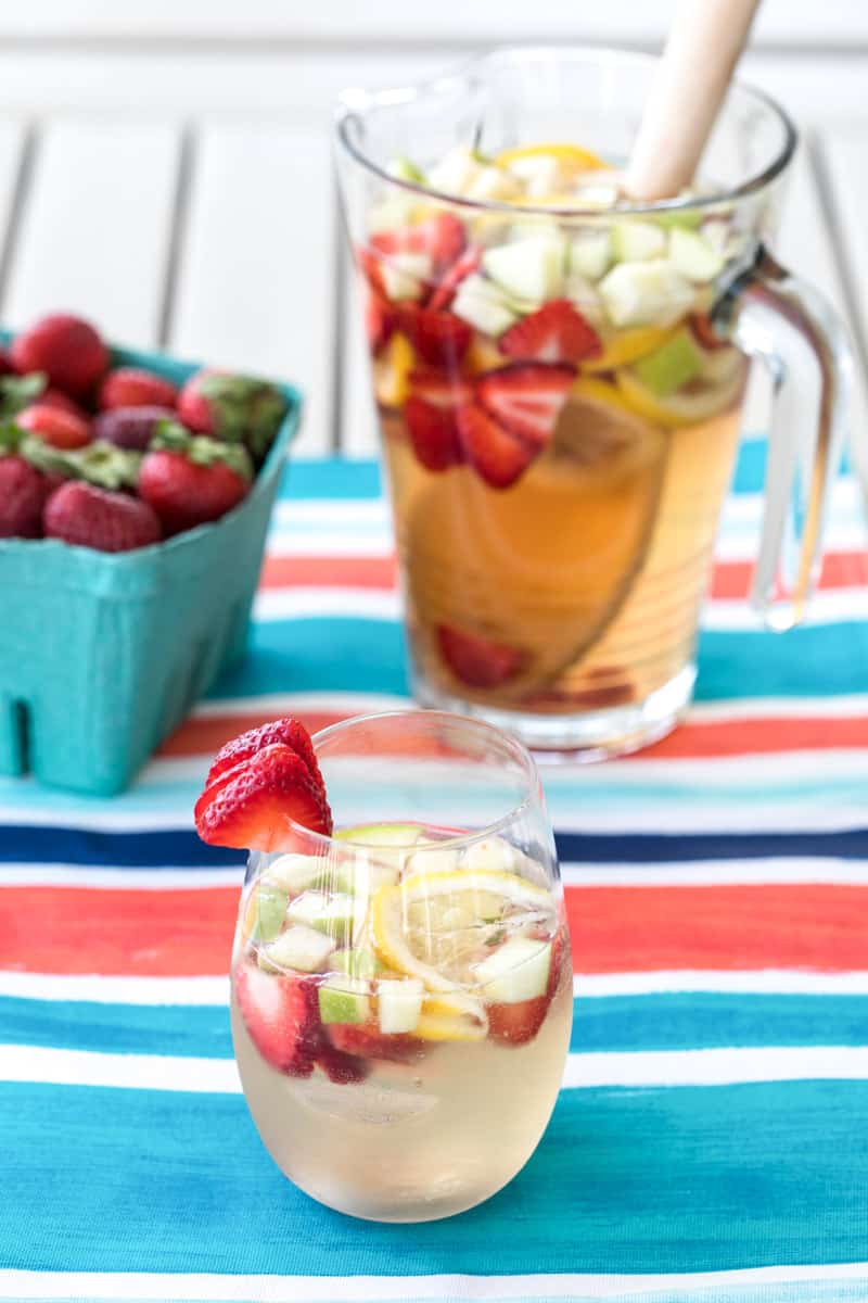 white wine sangria in a cup and a pitcher with strawberries, green apple, and lemon