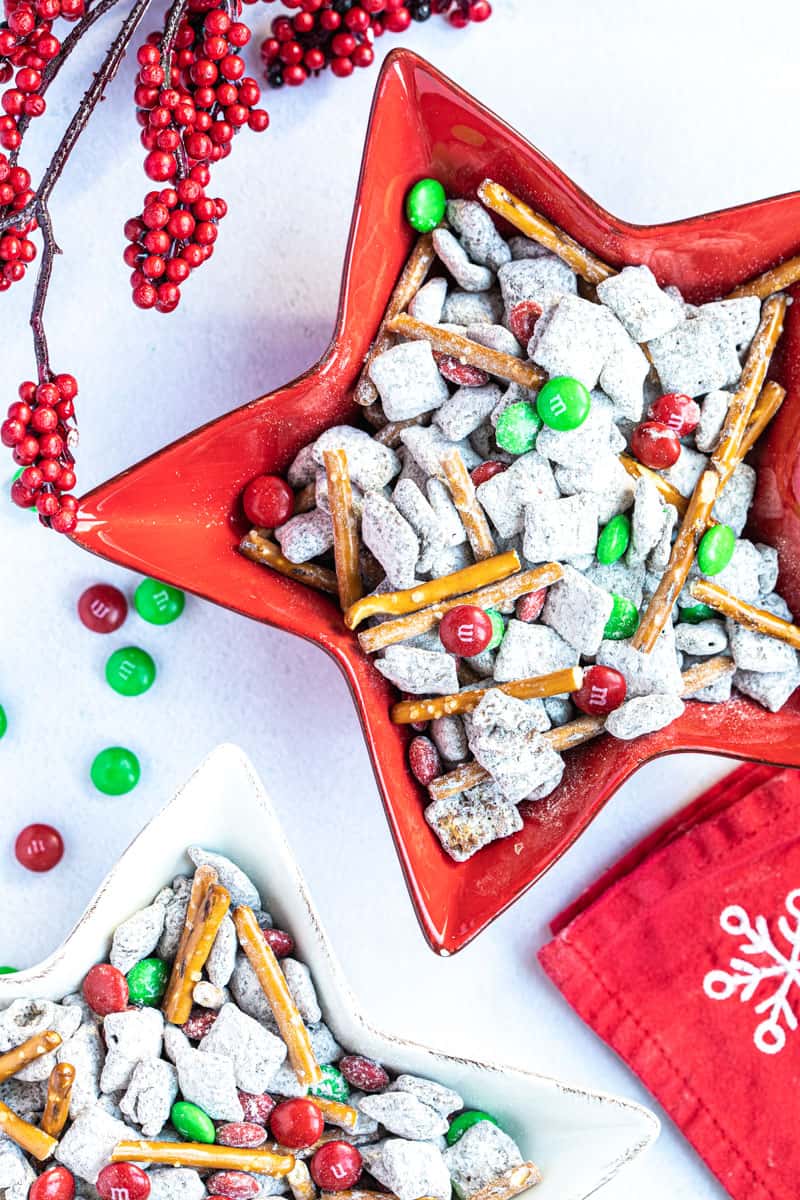 two bowls of Christmas puppy chow next to m&ms, holiday napkins, and decorations