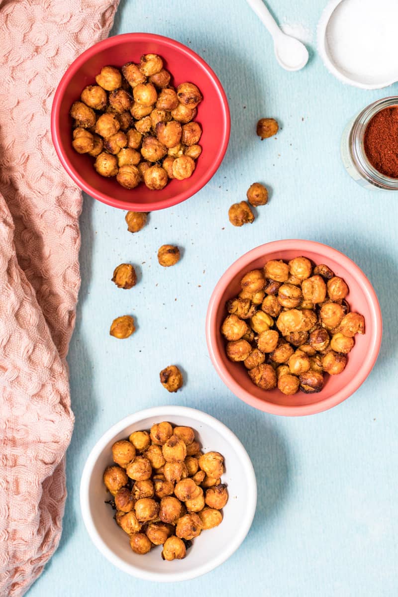 three bowls of air fried chickpeas next to spice jar and napkin