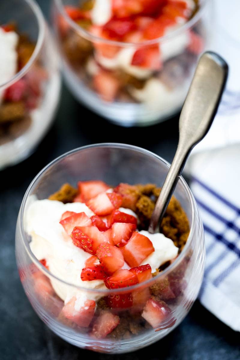 glass of strawberry parfait with mascarpone cream with spoon in front of two other glasses and kitchen towel 