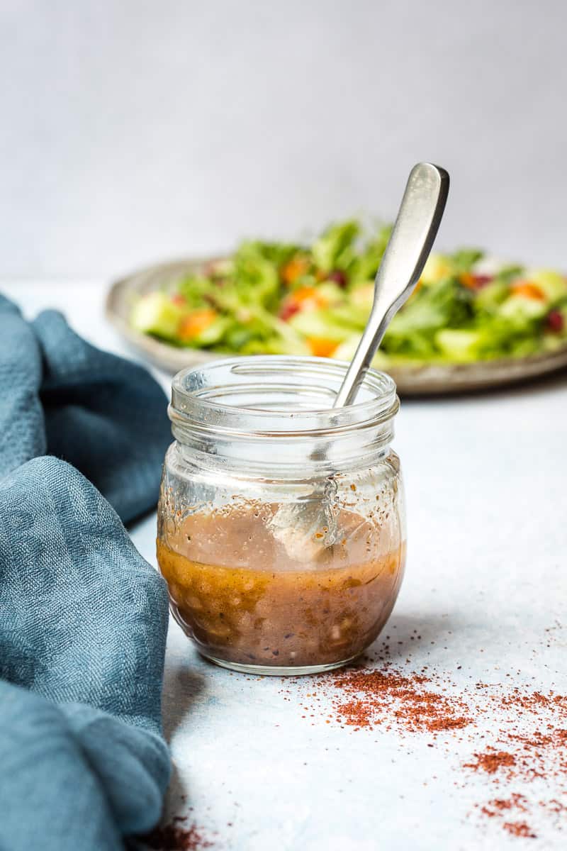 jar of sumac dressing next to blue towel and in front of plate with salad