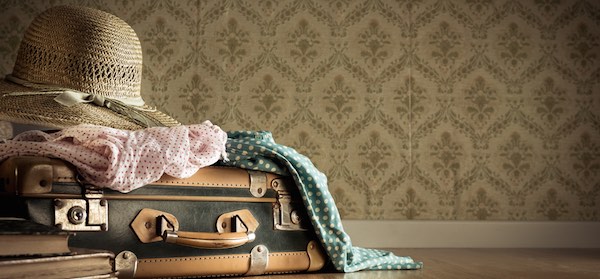 vintage suitcase with clothes on top sitting in front of retro wallpaper